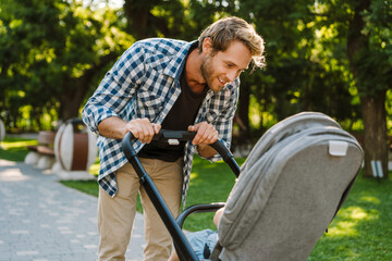 White father smiling while walking with her son in baby carriage at park