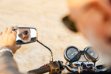 Bold senior man looking at rear-view mirror while riding motorcycle