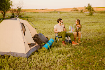 White couple eating sandwiches while resting during camping together - obrazy, fototapety, plakaty