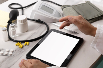 Doctor using and touching blank screen of pc tablet for online medical consultation.Different pills,bottles and blood pressure monitor on the white desk