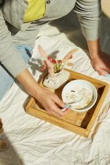 Woman in jeans sitting on the bed, and eating healthy granola bowl during the morning sunlight, breakfast in the bed.