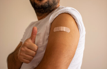 Man showing thumb up and his armwith bandage after got vaccinated or inoculation delta variant vaccine.