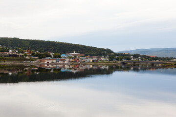 Naklejka na ściany i meble Panoramic view of a small town and its reflection in a body of water during a grey morning, Gaspé, Quebec, Canada