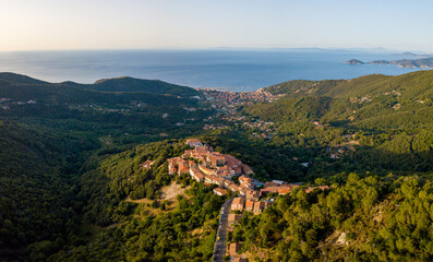 Fototapeta premium Aerial Drone Panorama of mountain old town Marciana on the islands of Elba Italy with green trees and the mediterranean sea ocean in the background