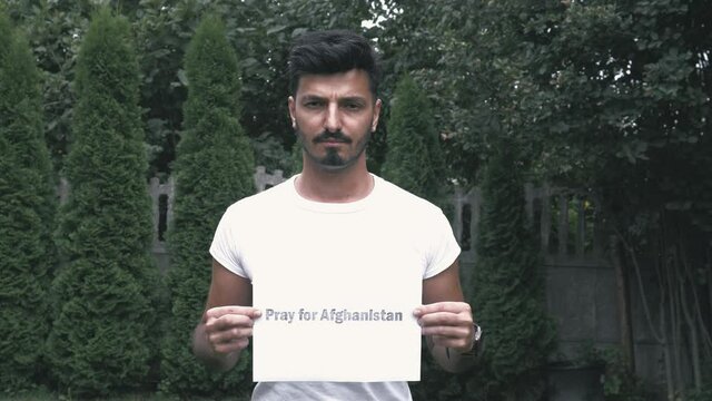 Pray for Afghanistan sign. The 
 muslim afghan man is holding a sign to save Afghanistan. A piece of paper request to pray for Afghanistan