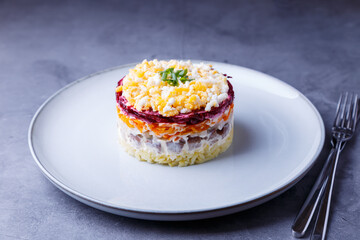 Herring salad under a fur coat. Traditional Russian multilayered salad from herring, beets, potatoes, carrots and eggs. Close-up, grey background.
