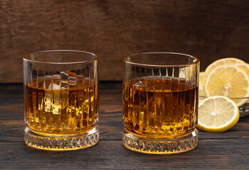 Whiskey or cognac or bourbon with ice on a wood background with lemon wedges