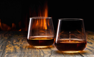 Two glasses of old cognac on the table in front of the fireplace - obrazy, fototapety, plakaty