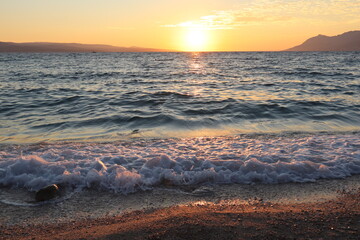Scenic sunset on the beach at the seaside, orange glare of the sun on the surface of the water and...