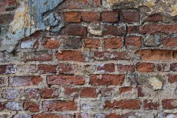 Texture of an old exterior wall surface made of red bricks. Bricks are aged and weathered with crumbled mortar and numerous cracks.