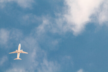 white passenger plane flies against the background of a bright blue sky with clouds