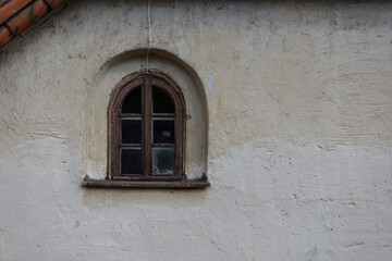 a small window of an old medieval house. a garland of diode lights hangs from the roof. the wall of the house is finished with gray plaster
