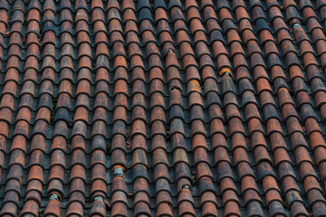 An old roof tiles pattern. Dark red weathered and aged tiles covering roof of old european house