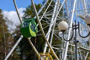 A booth on a Ferris wheel against a clear blue sky and trees in the park. Lightpost is in the foreground.
