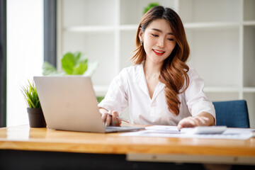 Young Asian businesswoman beautiful charming smiling and working with a computer laptop in the office. doing Financial analysis reports the graph of the company's and growth Market research.
