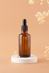 Amber glass dropper bottle with black lid on white podium for product presentation on beige background with dry plants. Skincare products ,natural cosmetic. Beauty concept for face and body care