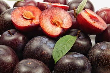 Whole ripe purple-red plums and plum halves, background