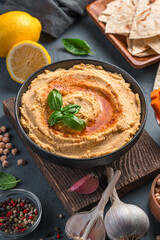 Hummus with olive oil and paprika on the background of ingredients. Side view, vertical.
