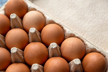brown hen eggs in a box made of recycled cardboard are located on a grey wooden countertop in the kitchen. Top view