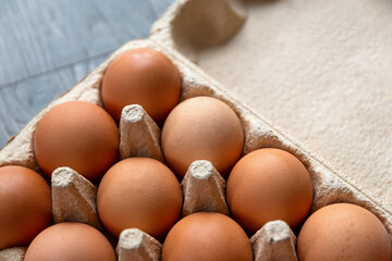 Closeup shot of set of brown chicken eggs in a recycled cardboard box. Box with eggs is on the grey wooden surface in the kitchen.