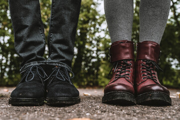 Burgundy leather boots. Blue suede shoes. Man and woman in casual footwear. Asphalt with fallen leaves. Autumn fashion.