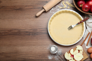 Flat lay composition with raw dough, fork and ingredients on wooden table, space for text. Baking apple pie