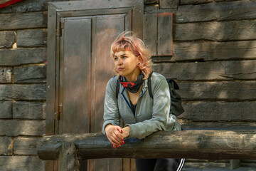 Mujer apoyada en un tronco de madera junto a una cabaña, chica de pelo rosa pensativa fuera de la...