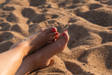 A woman stretched out her legs on the beachю Naked female feet of a middle-aged woman on the sand on the beach during sunset. Hobby and leisure