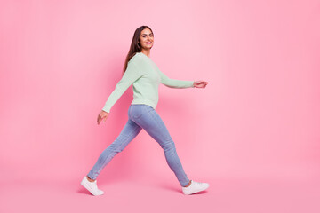 Fototapeta na wymiar Full length profile photo of cheerful young brunette lady go wear pullover jeans sneakers isolated on pink background