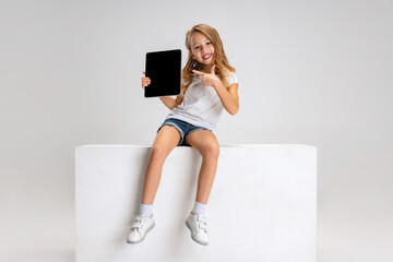 Portrait of little cute girl in casual clothes sitting on big box isolated on white studio...