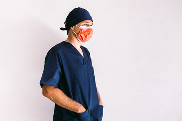 Male nurse, doctor or veterinarian wearing red mask and dark blue uniform in hospital, hands in pockets, smiling. Medicine, hospital and healthcare concept.