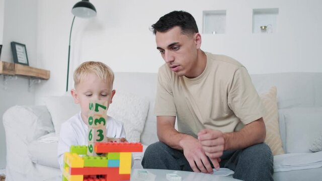 A father playing with his son holding a constructor sitting on the sofa