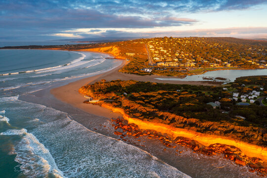 Aerial view of a rugged coastline below a town catching golden dawn side lighting