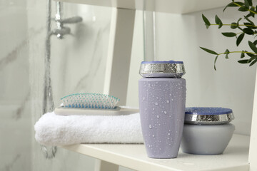 Hair care cosmetic products, towel and brush on white shelf indoors