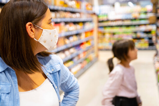 Side view photo of two female person mom in a medical mask and daughter inside the store looking at the shelves with products.