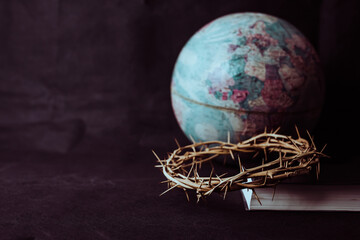 the crown of thorns of Jesus on  the holy bible with blurred world globe on black background...