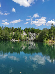The shore of the lake Light with turquoise water, which reflects the trees and the sky with clouds, in the mountain park Ruskeala.