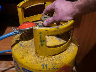 Caucasian man opens the pressure valve on yellow household natural gas tank .
