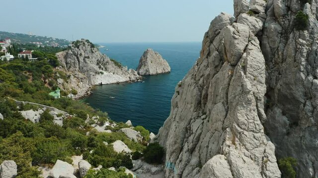 Aerial close fly behind rock Krylo Lebedya - Swan Wing with Diva rock and black sea in background. Crimea, Simeiz. Summer travel tourism concept