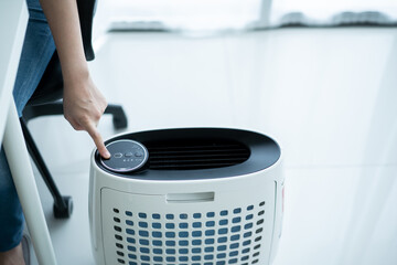 Asian woman turning on and using the modern air purifier while staying in the living room.