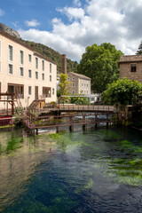 Fototapeta na wymiar Fontaine-de-Vaucluse old town with river Sorgue in the foreground, charming medieval village in Vaucluse, Provence, southern France