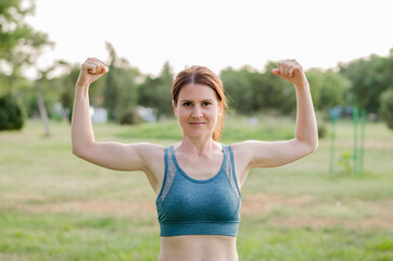 The athlete demonstrates the muscles of the arms in nature. Athletic young woman shows biceps. Healthy lifestyle