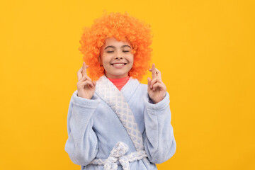 dreamy kid in fancy orange wig hair wear home bathrobe making wish, crossed finger