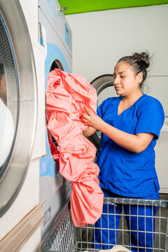 Woman standing in front of a washing machine picking up a sheet in a laundry