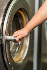Man's hand opening the door of an industrial laundry washing machine