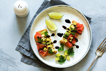 Avocado and salmon sandwiches with balsamic sauce and cilantro on old olive board. Top view