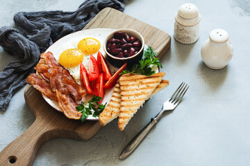 Full fry up traditional English breakfast with fried eggs, sausages, bacon, black pudding, beans, toasts and tea on gray concrete background. Top view