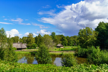 Fototapeta na wymiar Green landscape with lake, cabins and blue sky with approaching storm.