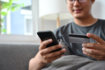 Closed up with Asian man holding a credit card while shopping online with his smartphone.