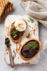 Sandwich with slice of mozzarella cheese and tapenade, caper on light grey rustic table background. Traditional Provence dish. Selective focus
